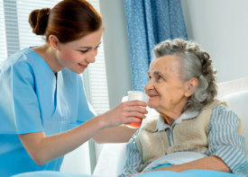 caregiver helping old woman drink a glass of juice